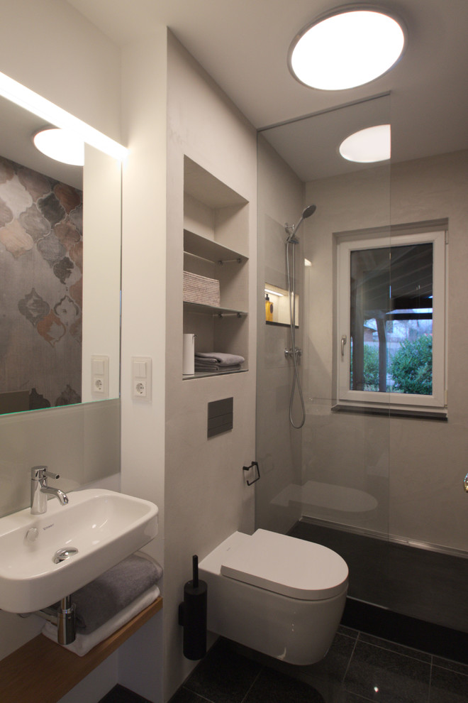 Inredning av ett modernt litet badrum med dusch, med öppna hyllor, en öppen dusch, en vägghängd toalettstol, grå väggar, ett väggmonterat handfat och beiget golv