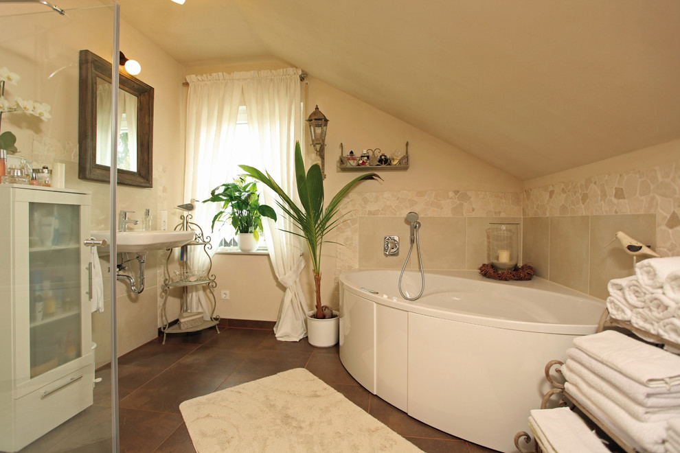 Immagine di una stanza da bagno country con ante di vetro, ante bianche, vasca ad angolo, piastrelle beige, pareti beige, pavimento in terracotta, lavabo sospeso e pavimento marrone