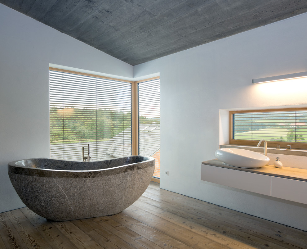 Modern inredning av ett stort brun brunt badrum, med släta luckor, vita skåp, ett fristående badkar, vita väggar, mellanmörkt trägolv, ett fristående handfat, träbänkskiva och brunt golv