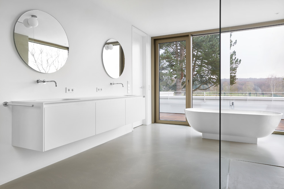 Inspiration för mellanstora moderna vitt badrum med dusch, med släta luckor, vita skåp, ett fristående badkar, en kantlös dusch, vita väggar, betonggolv, bänkskiva i akrylsten, med dusch som är öppen, ett väggmonterat handfat och grått golv