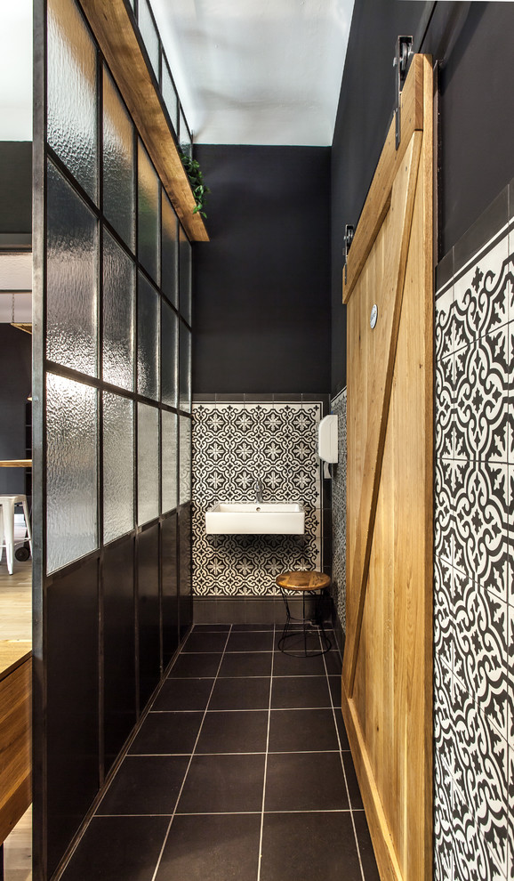 Foto på ett industriellt badrum, med svart och vit kakel, keramikplattor, svarta väggar, ett väggmonterat handfat och svart golv