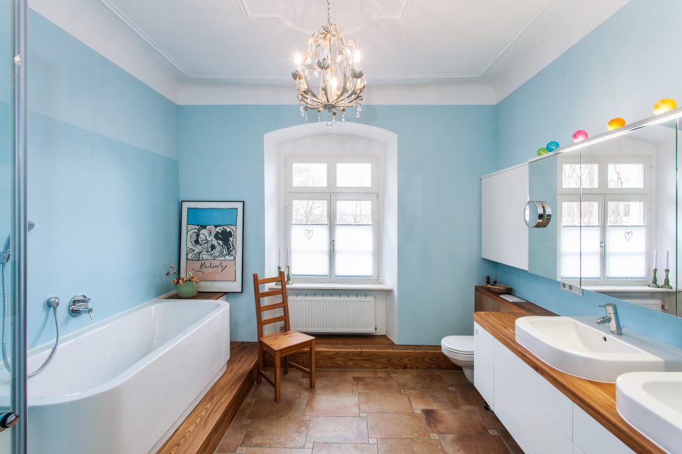 Пример оригинального дизайна: ванная комната среднего размера в стиле кантри с белыми фасадами, инсталляцией, коричневой плиткой, синими стенами, полом из терракотовой плитки, столешницей из дерева, коричневым полом, коричневой столешницей, плоскими фасадами, ванной в нише, угловым душем, накладной раковиной и душем с распашными дверями