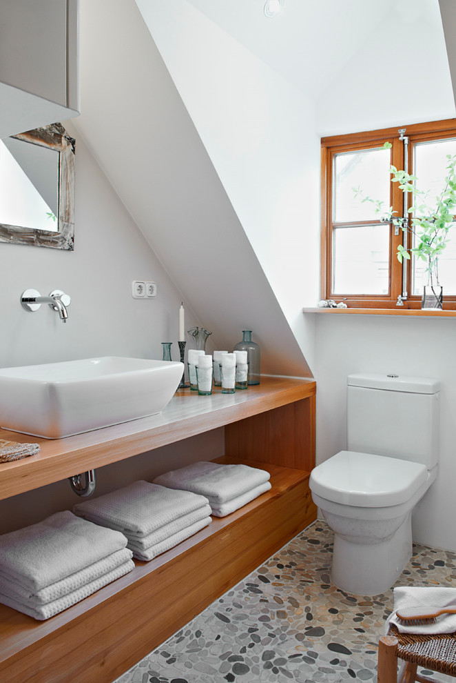 Cette image montre une petite salle de bain rustique avec WC séparés, une plaque de galets, un mur blanc et un sol en galet.