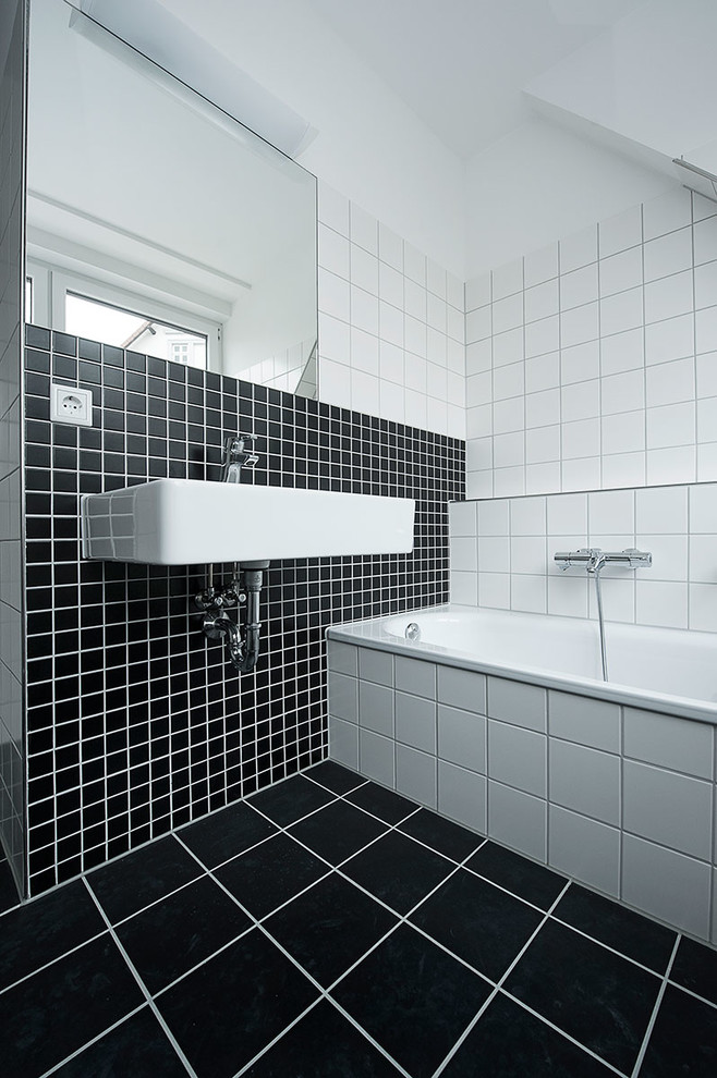Inredning av ett modernt badrum, med ett väggmonterat handfat, ett badkar i en alkov, svart och vit kakel, vita väggar och keramikplattor