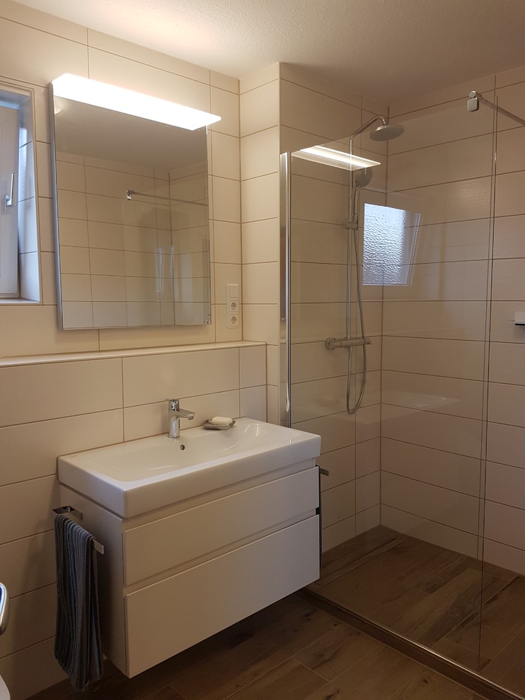 Inredning av ett modernt litet badrum med dusch, med beige skåp, en öppen dusch, en toalettstol med separat cisternkåpa, vit kakel, porslinskakel, vita väggar, klinkergolv i porslin, ett avlångt handfat, brunt golv och med dusch som är öppen