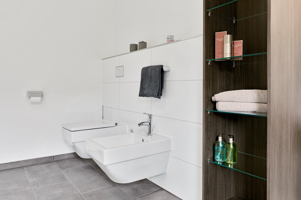 Inredning av ett modernt stort vit vitt badrum med dusch, med släta luckor, bruna skåp, en vägghängd toalettstol, vit kakel, porslinskakel, vita väggar, träbänkskiva och grått golv