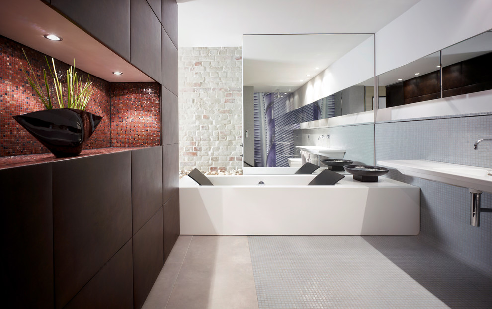 Immagine di una grande stanza da bagno minimal con ante lisce, ante nere, vasca da incasso, piastrelle grigie, piastrelle a mosaico, pareti bianche, pavimento con piastrelle a mosaico e lavabo integrato