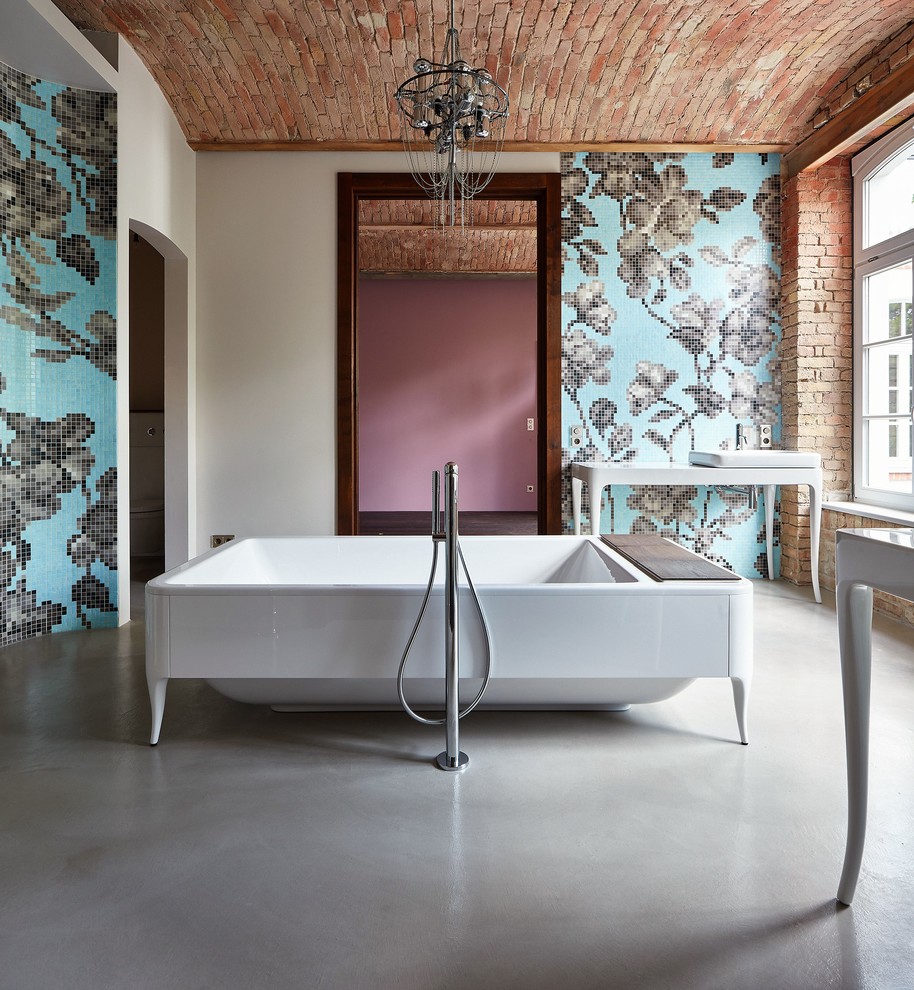 Foto de cuarto de baño principal ecléctico grande con bañera exenta, baldosas y/o azulejos de vidrio, suelo de cemento y lavabo sobreencimera