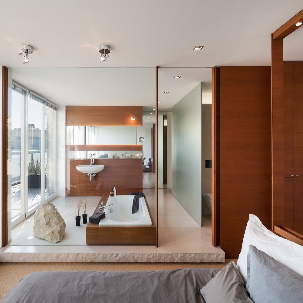 Modern inredning av ett mellanstort en-suite badrum, med ett väggmonterat handfat, ett platsbyggt badkar, en vägghängd toalettstol, beige kakel, stenhäll och grå väggar