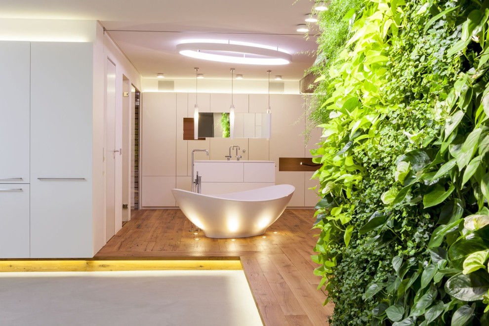 Modernes Duschbad mit weißen Schränken, freistehender Badewanne, weißer Wandfarbe, braunem Holzboden und Pflanzen in Stuttgart