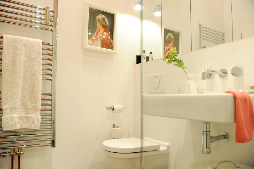 Inredning av ett modernt mellanstort badrum med dusch, med släta luckor, en kantlös dusch, en vägghängd toalettstol, vit kakel, keramikplattor, vita väggar, cementgolv, ett väggmonterat handfat och med dusch som är öppen