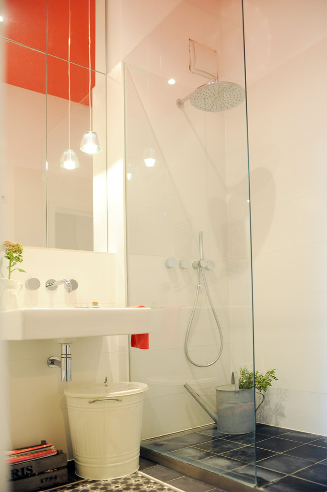 Bild på ett mellanstort funkis badrum med dusch, med släta luckor, en kantlös dusch, en vägghängd toalettstol, vit kakel, keramikplattor, vita väggar, cementgolv, ett väggmonterat handfat och med dusch som är öppen