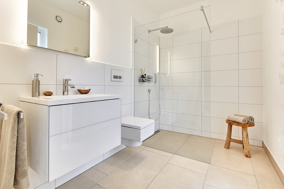 Nordisk inredning av ett badrum med dusch, med släta luckor, vita skåp, våtrum, vit kakel, vita väggar, ett integrerad handfat, beiget golv, med dusch som är öppen, en vägghängd toalettstol, keramikplattor och cementgolv