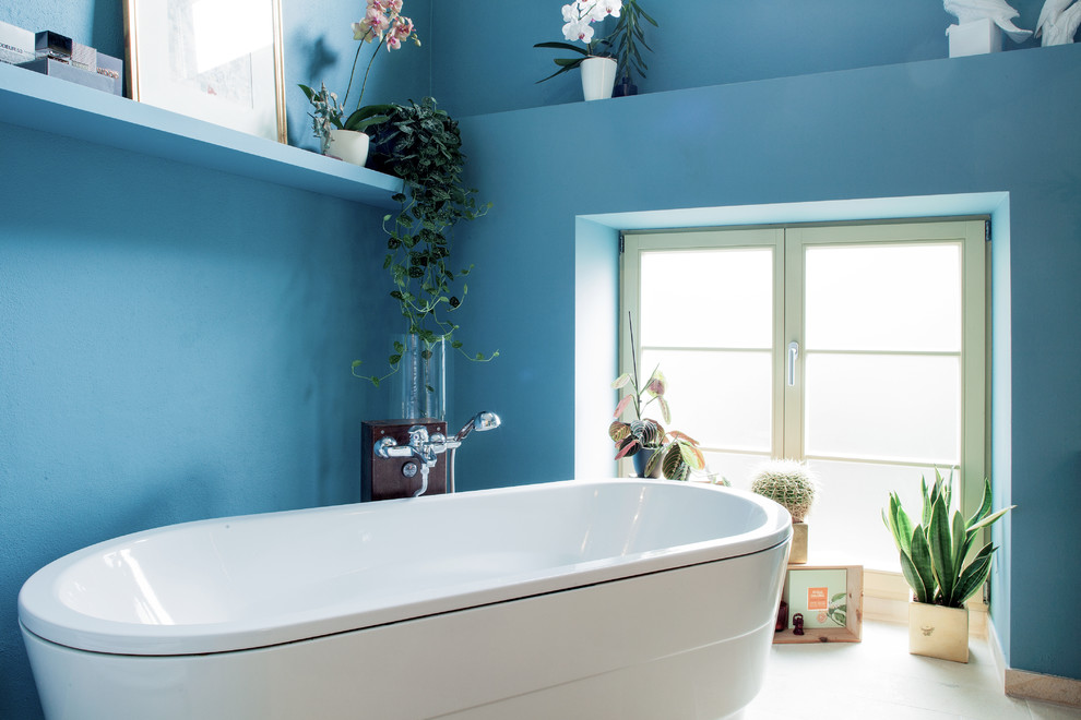 Imagen de cuarto de baño principal contemporáneo de tamaño medio con bañera exenta, paredes azules, suelo de piedra caliza y ventanas