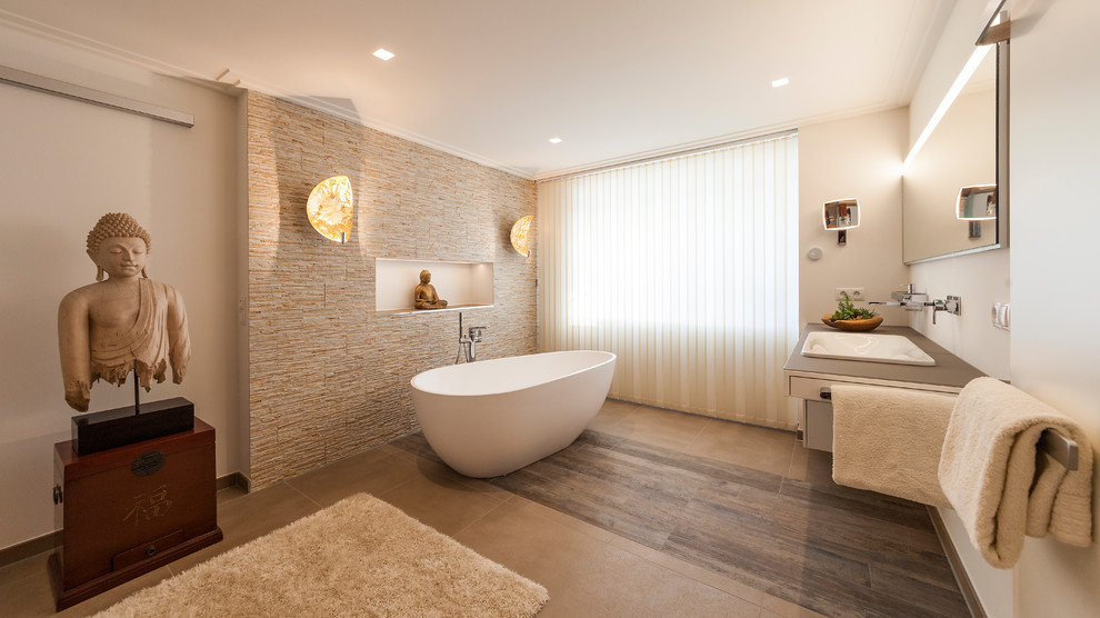 Cette image montre une salle de bain principale asiatique de taille moyenne avec une baignoire indépendante, un carrelage beige, un mur beige, un lavabo posé, un sol beige, un placard à porte plane, des portes de placard blanches, un carrelage de pierre et un mur en pierre.