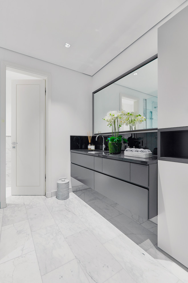 Immagine di una stanza da bagno minimalista di medie dimensioni con ante lisce, ante grigie, pareti bianche, pavimento in marmo, lavabo integrato, pavimento bianco e top grigio