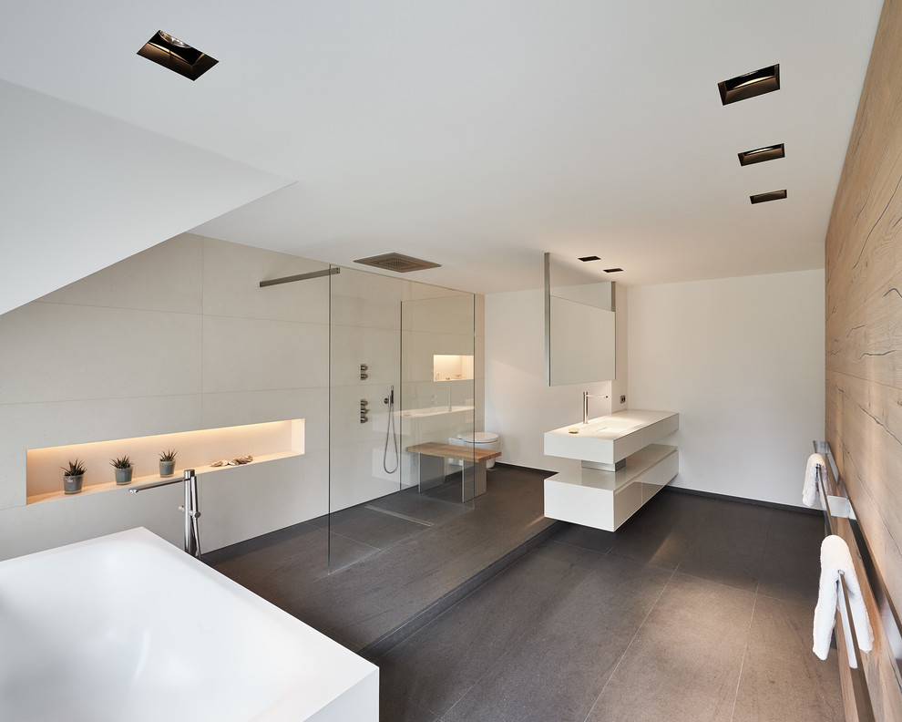 Design ideas for a large modern ensuite bathroom in Dusseldorf with white cabinets, a freestanding bath, a built-in shower, white walls, a console sink, flat-panel cabinets, a wall mounted toilet, porcelain tiles, porcelain flooring, solid surface worktops and an open shower.