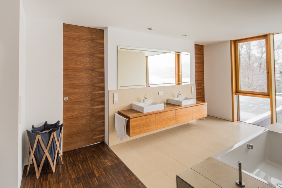 Aménagement d'une salle de bain moderne avec une vasque, une baignoire posée, une douche à l'italienne, un carrelage beige et un carrelage de pierre.