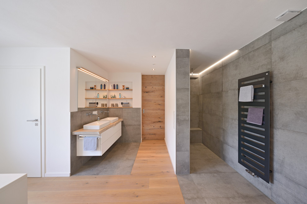 Inredning av ett modernt stort badrum med dusch, med släta luckor, vita skåp, en kantlös dusch, svart kakel, stenhäll, vita väggar, mellanmörkt trägolv, ett fristående handfat, träbänkskiva och med dusch som är öppen