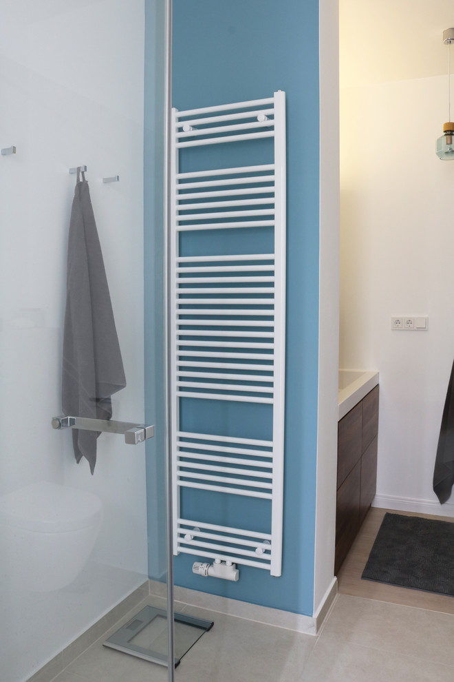 Bild på ett mellanstort funkis badrum, med släta luckor, skåp i mörkt trä, ett platsbyggt badkar, en vägghängd toalettstol, beige kakel, blå väggar, bambugolv, ett konsol handfat, bänkskiva i akrylsten och vitt golv