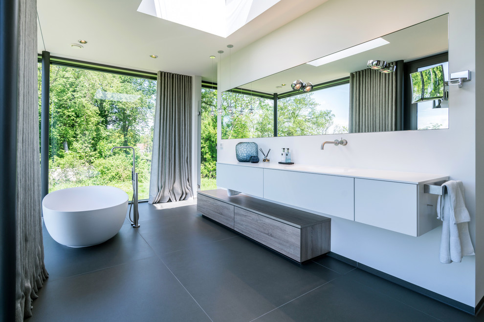 Inspiration för stora moderna vitt en-suite badrum, med släta luckor, ett fristående badkar, vita väggar, ett integrerad handfat, svart golv och vita skåp