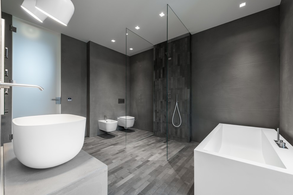 Idéer för ett stort modernt grå badrum med dusch, med ett fristående badkar, en kantlös dusch, en vägghängd toalettstol, grå kakel, grå väggar, ett fristående handfat, bänkskiva i betong, grått golv, med dusch som är öppen, grå skåp, stickkakel och betonggolv