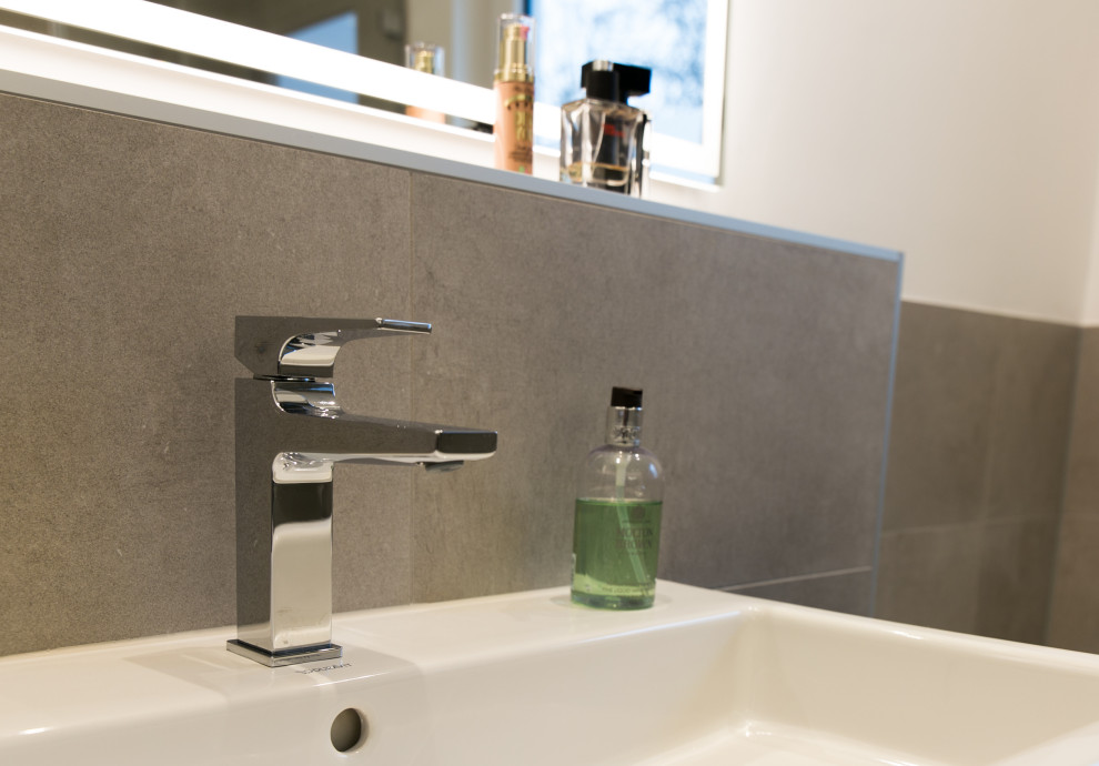 Modernes Badezimmer mit weißen Schränken, grauen Fliesen, grauer Waschtischplatte und Einzelwaschbecken in Frankfurt am Main