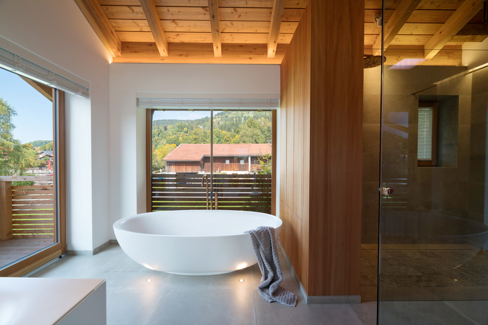Idée de décoration pour une salle d'eau design en bois brun de taille moyenne avec un placard à porte plane, une baignoire indépendante, un espace douche bain, un carrelage gris, un mur blanc et un sol gris.