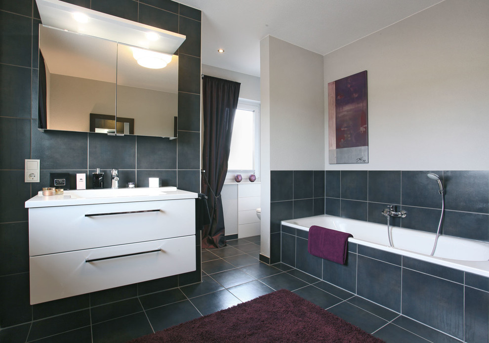 Modernes Badezimmer mit weißen Schränken, Einbaubadewanne, grauen Fliesen, beiger Wandfarbe, grauem Boden und weißer Waschtischplatte in Sonstige