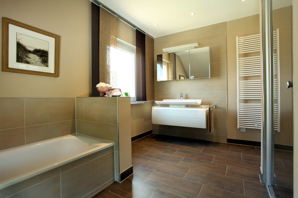 Modernes Badezimmer mit weißen Schränken, Einbaubadewanne, bodengleicher Dusche, beigen Fliesen, beiger Wandfarbe, braunem Boden und weißer Waschtischplatte in Sonstige