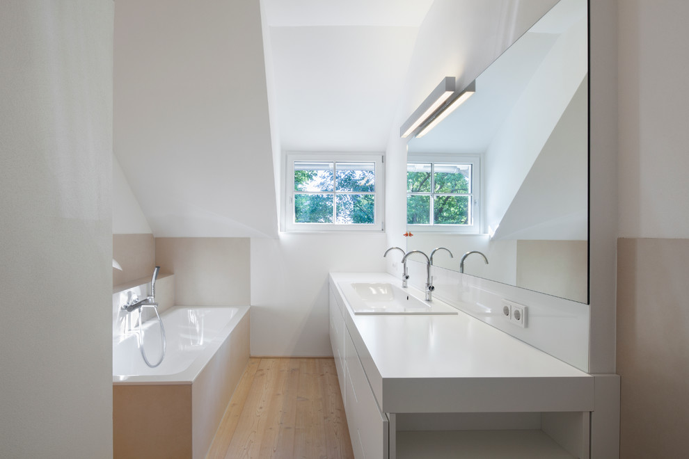 Photo of a medium sized contemporary bathroom in Dusseldorf with flat-panel cabinets, white cabinets, a built-in bath, white walls, medium hardwood flooring and a trough sink.