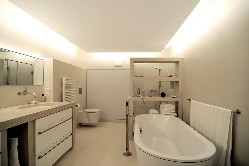 Идея дизайна: большая ванная комната в современном стиле с плоскими фасадами, белыми фасадами, отдельно стоящей ванной, угловым душем, инсталляцией, серыми стенами, бетонным полом, врезной раковиной и столешницей из бетона