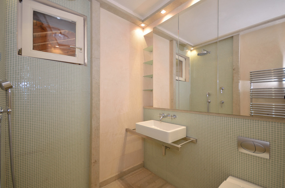 Modern inredning av ett litet badrum med dusch, med en kantlös dusch, en vägghängd toalettstol, blå kakel, mosaik, beige väggar, kalkstensgolv, ett fristående handfat, bänkskiva i rostfritt stål, beiget golv och med dusch som är öppen
