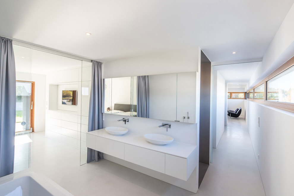 Modernes Badezimmer mit flächenbündigen Schrankfronten, weißen Schränken, weißer Wandfarbe, Betonboden, Aufsatzwaschbecken, grauem Boden und weißer Waschtischplatte in Sonstige
