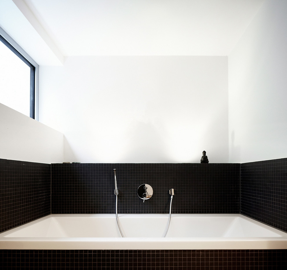 Modern inredning av ett badrum, med ett platsbyggt badkar, svart kakel och mosaik