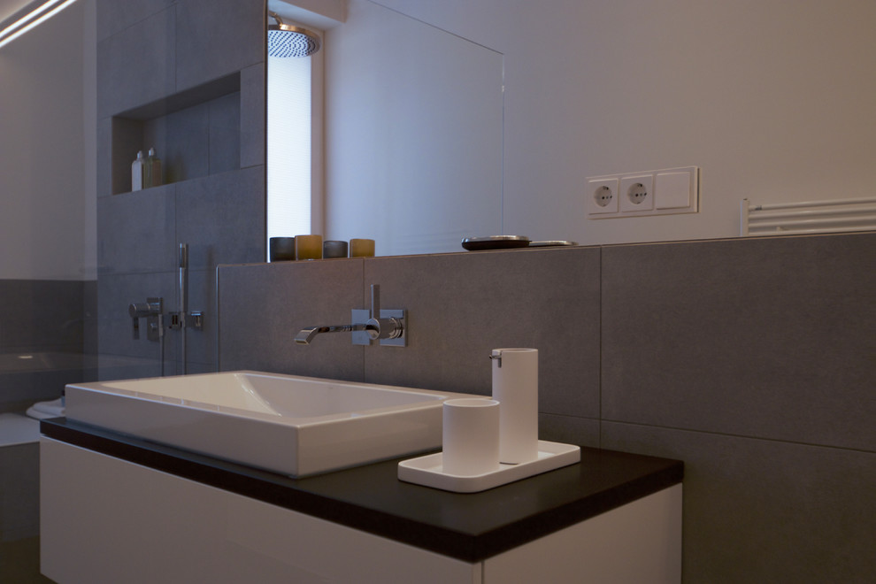 Exempel på ett mellanstort modernt badrum med dusch, med vita skåp, ett platsbyggt badkar, en öppen dusch, en vägghängd toalettstol, grå kakel, vita väggar, ett fristående handfat, grått golv och med dusch som är öppen