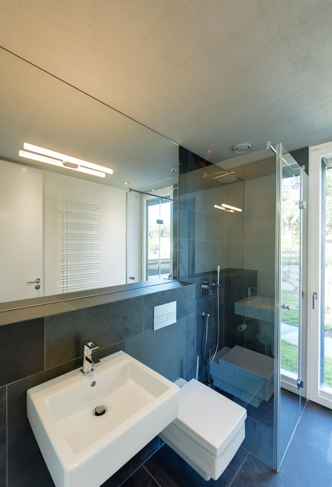 Cette image montre une salle d'eau design de taille moyenne avec WC suspendus, un carrelage noir, un mur noir, un sol en ardoise, une douche à l'italienne, un carrelage de pierre et un lavabo suspendu.