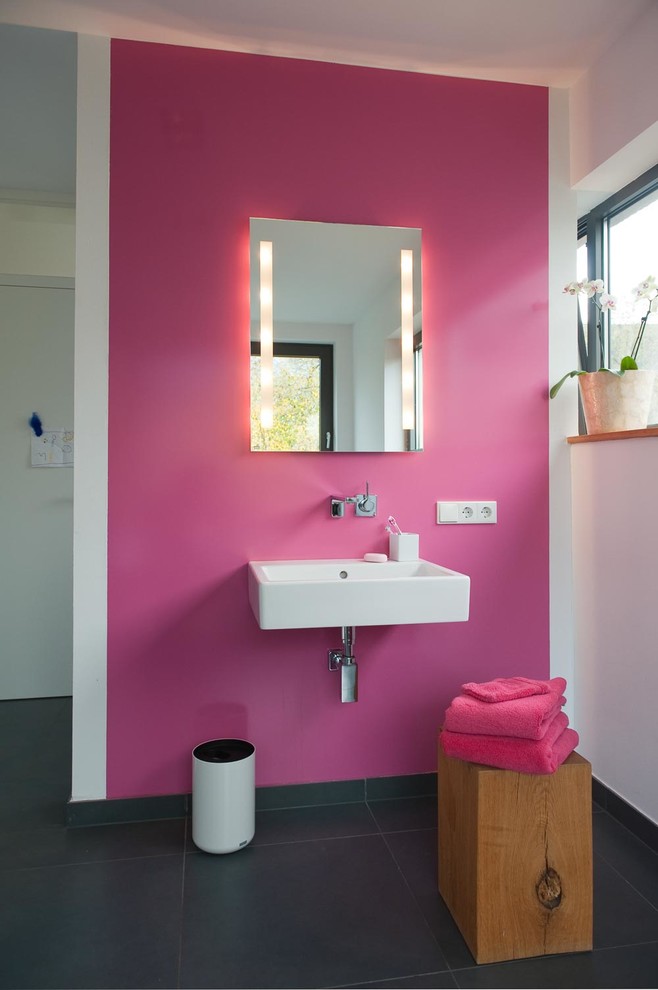 Foto de cuarto de baño rectangular contemporáneo de tamaño medio con baldosas y/o azulejos grises, paredes rosas, lavabo suspendido, baldosas y/o azulejos de piedra y espejo con luz
