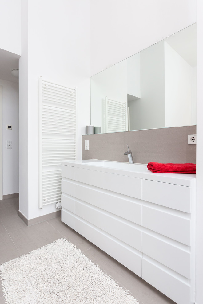 Inspiration för ett mellanstort funkis badrum, med ett integrerad handfat, släta luckor, vita skåp, grå kakel, vita väggar och stenhäll