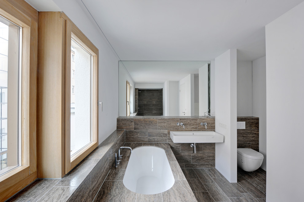 Kleines Modernes Badezimmer mit Einbaubadewanne, Wandtoilette, braunen Fliesen, Steinfliesen, weißer Wandfarbe und Wandwaschbecken in Berlin