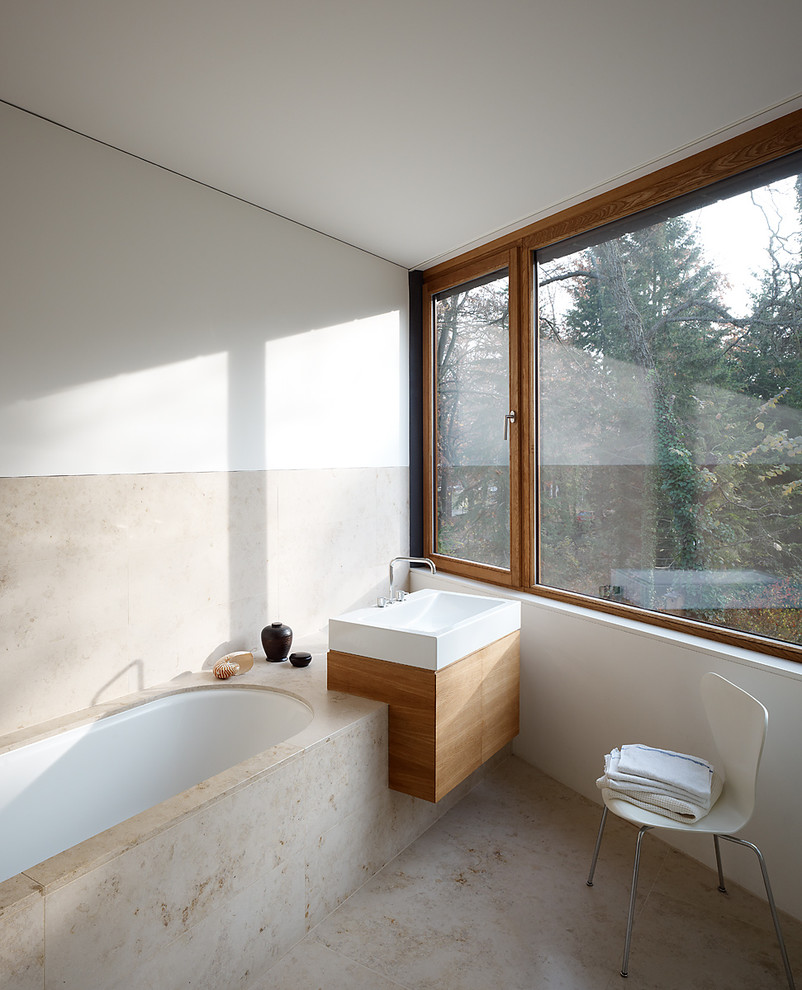 Modern inredning av ett mellanstort badrum, med släta luckor, skåp i mellenmörkt trä, ett undermonterat badkar, beige kakel, stenhäll, vita väggar, travertin golv, ett fristående handfat och träbänkskiva