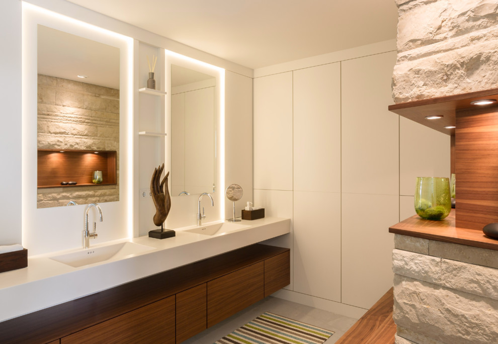 Foto de cuarto de baño contemporáneo de tamaño medio con lavabo integrado, armarios con paneles lisos, puertas de armario de madera oscura, paredes blancas y espejo con luz