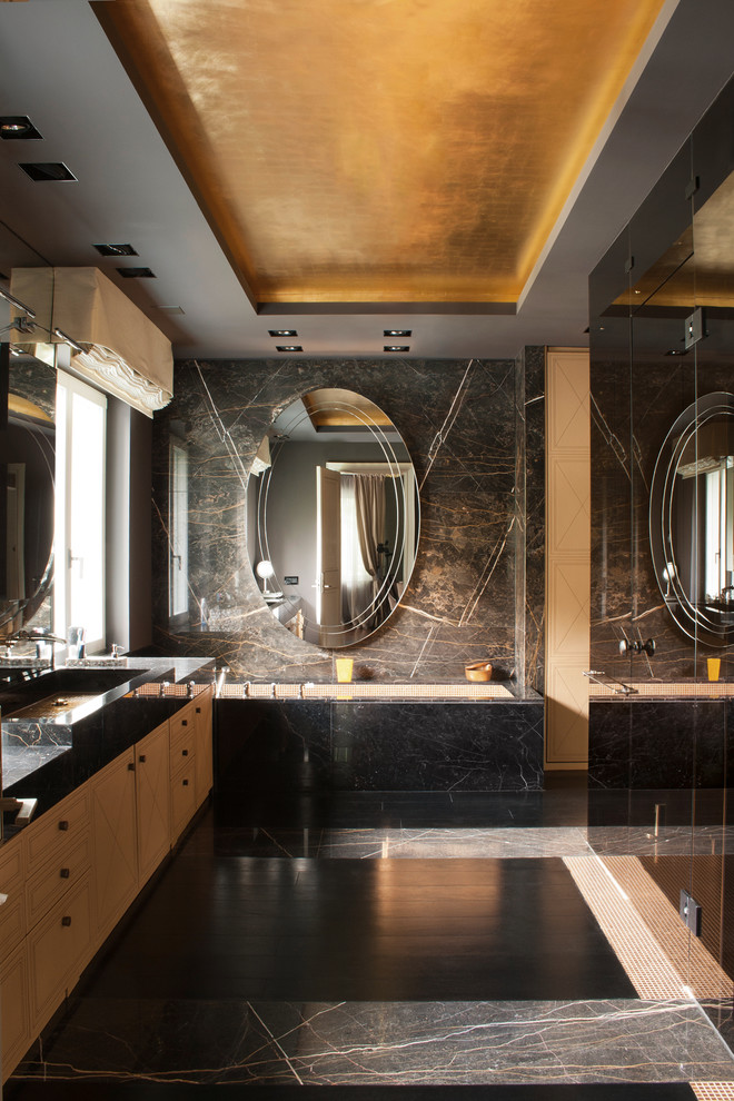 Example of a trendy stone slab marble floor drop-in bathtub design in Berlin with raised-panel cabinets, light wood cabinets, an integrated sink and marble countertops