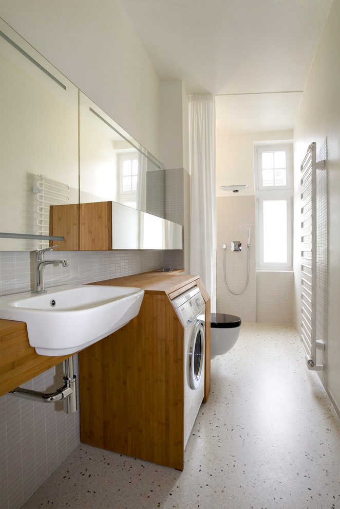 Example of a mid-sized trendy 3/4 gray tile and matchstick tile bathroom design in Berlin with flat-panel cabinets, medium tone wood cabinets, wood countertops, white walls and a drop-in sink