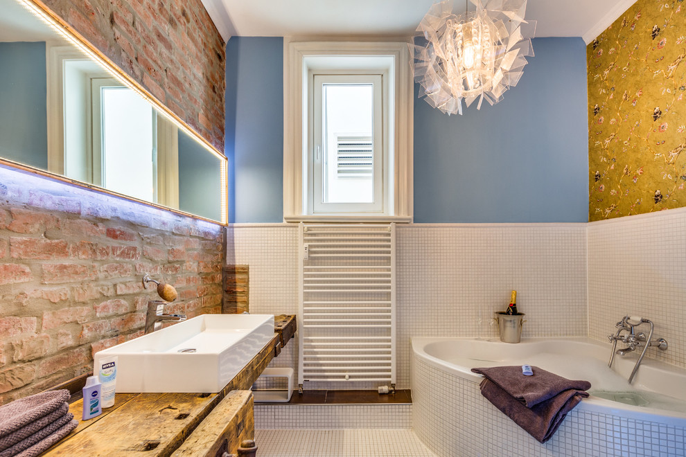 Foto på ett stort funkis badrum, med ett hörnbadkar, vit kakel, mosaik, blå väggar, mosaikgolv, ett fristående handfat och träbänkskiva