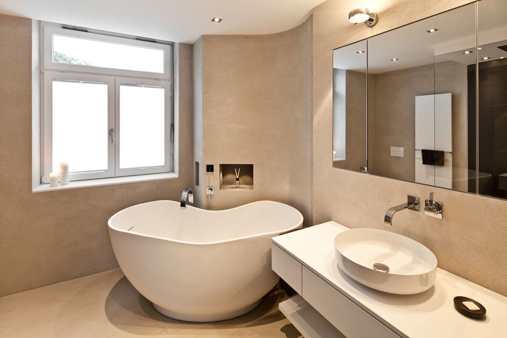 Modern inredning av ett mellanstort badrum med dusch, med en öppen dusch, betonggolv, ett fristående handfat, granitbänkskiva, släta luckor, vita skåp, ett fristående badkar och beige väggar