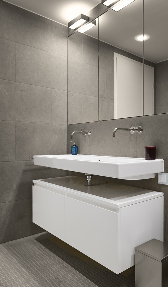 Modernes Badezimmer mit profilierten Schrankfronten, weißen Schränken, grauen Fliesen, grauer Wandfarbe, Waschtischkonsole, grauem Boden, weißer Waschtischplatte, Einbaubadewanne, Steinfliesen und Mosaik-Bodenfliesen in München