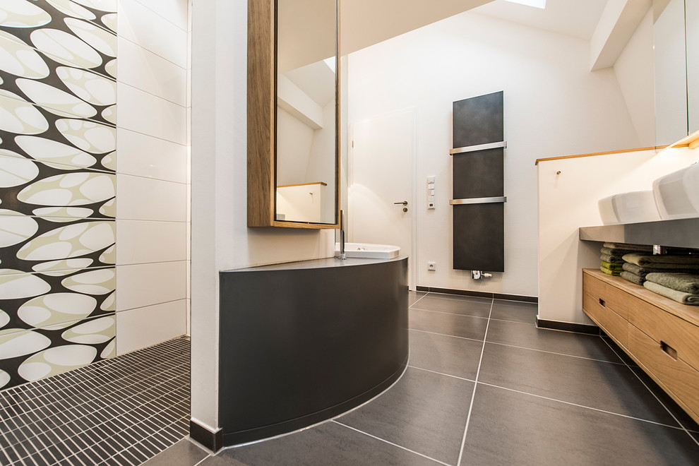 Design ideas for a medium sized contemporary bathroom in Berlin with medium wood cabinets, solid surface worktops, a corner bath, grey tiles, ceramic tiles, a vessel sink, a built-in shower, a wall mounted toilet, white walls, ceramic flooring and flat-panel cabinets.