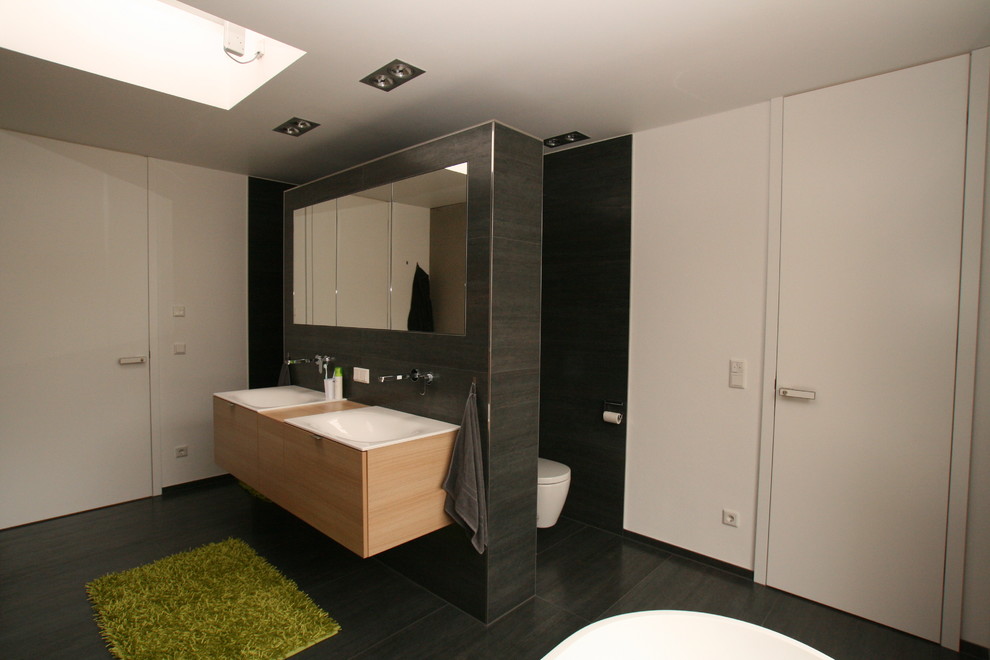 Idéer för stora funkis badrum, med skåp i ljust trä, svart kakel, svarta väggar, ett integrerad handfat, ett fristående badkar, en kantlös dusch, svart golv och med dusch som är öppen