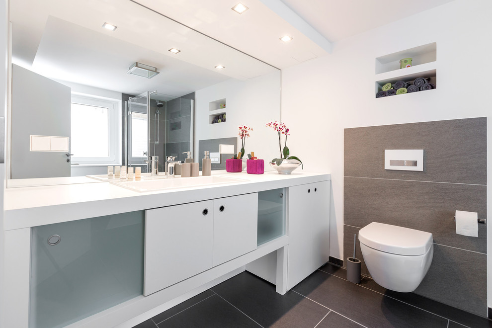 Inspiration for a medium sized contemporary ensuite bathroom in Hanover with white cabinets, a wall mounted toilet, grey tiles, cement tiles, white walls, a built-in sink and solid surface worktops.